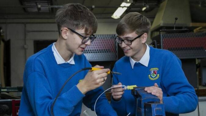 Zwei Schüler des St. Finian’s Community College untersuchen gemeinsam etwas konzentriert im Werkstattbereich.