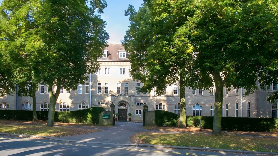 Der Campus von St. Francis' College zeigt ein historisches Gebäude umgeben von grünen Bäumen und einem gepflasterten Weg zum Eingang.