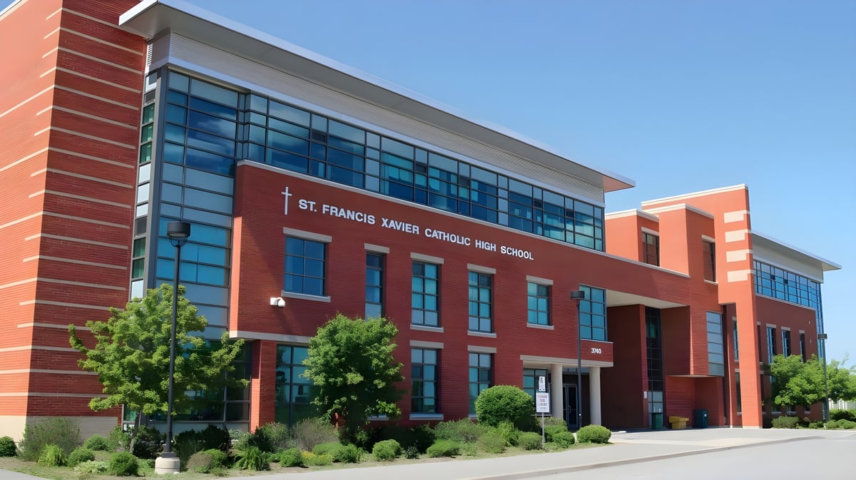 Das mehrstöckige Backsteingebäude der St. Francis Xavier High School mit großen Glasfenstern steht eingerahmt von Bäumen und Sträuchern.