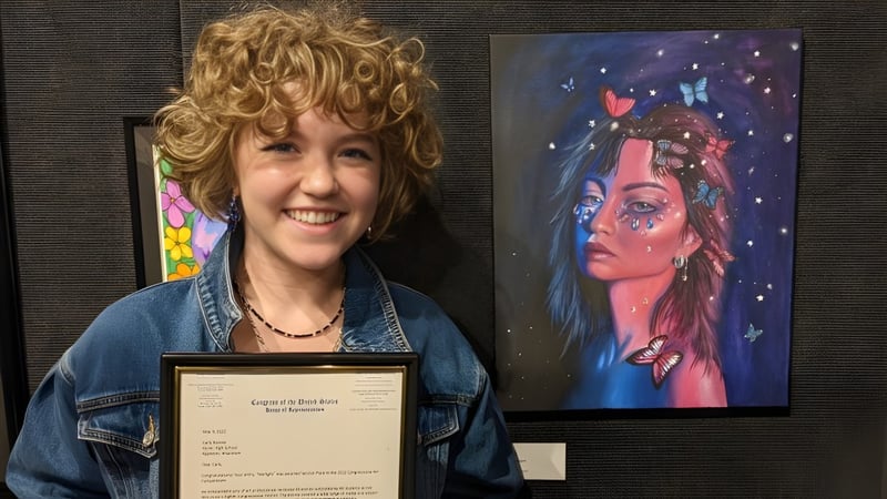 Eine Frau mit lockigen blonden Haaren steht vor einem farbenfrohen Gemälde auf dem Campus der St. Francis Xavier High School.