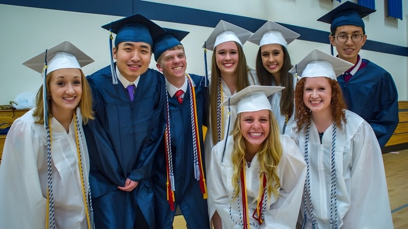 Eine Gruppe von Absolventinnen und Absolventen der St. Francis Xavier High School steht vor einer blau-weißen Wand.