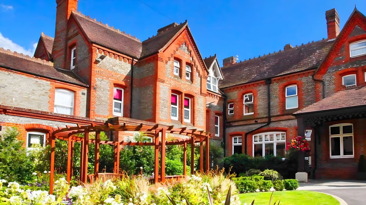 Das Backsteingebäude von St. George's Ascot ist von einem gepflegten Garten mit üppiger Bepflanzung umgeben.