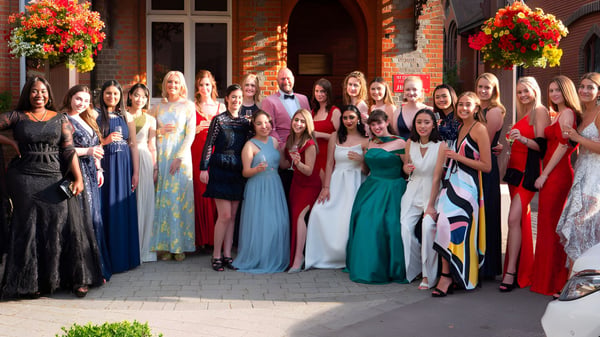 Eine Gruppe elegant gekleideter Personen steht vor einem Backsteingebäude auf dem Campus von St. George's Ascot.