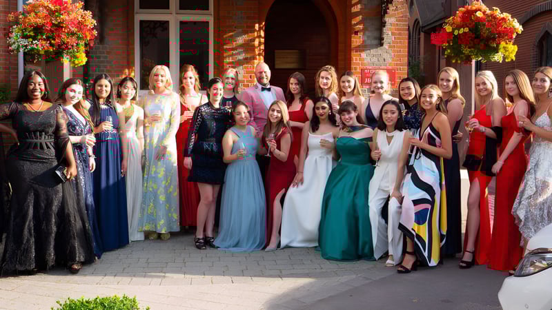 Eine Gruppe elegant gekleideter Personen steht vor einem Backsteingebäude auf dem Campus von St. George's Ascot.