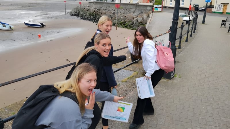 Eine Gruppe Schülerinnen der St. George's Ascot steht gemeinsam auf einem Gehweg nahe einem Gewässer mit felsiger Küste und Gebäuden im Hintergrund.