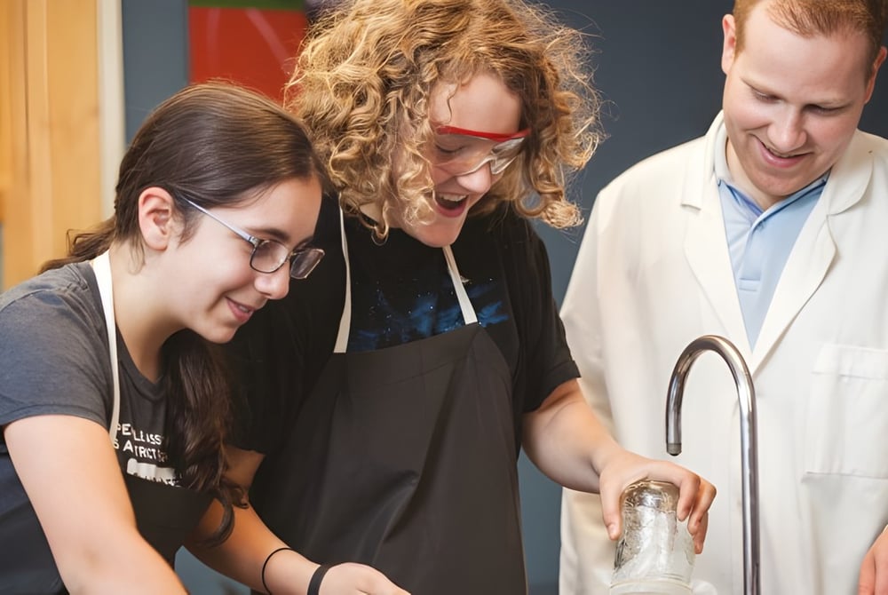 Drei Personen arbeiten gemeinsam in einem Labor der St. George's School of Montreal mit Regalen und Gerätschaften im Hintergrund.