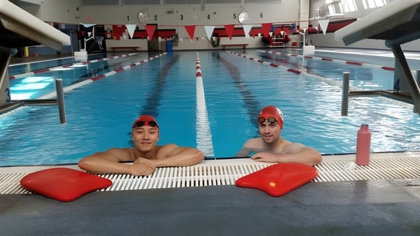 Zwei Schülerinnen mit roten Badekappen sitzen auf roten Schwimmbrettern im Schwimmbecken der St. George’s School.