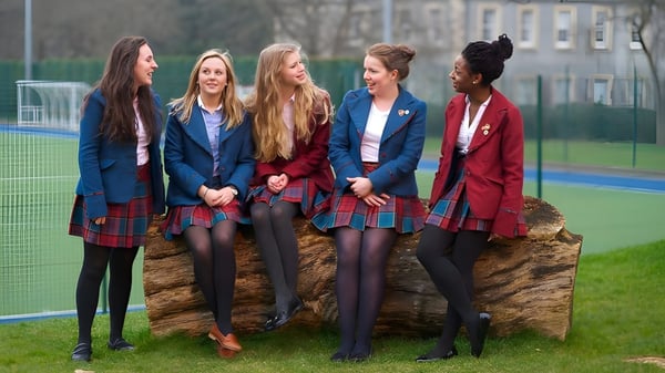 Eine Gruppe Schülerinnen der St. George's School in Schuluniform steht gemeinsam auf dem Sportfeld vor Gebäuden.