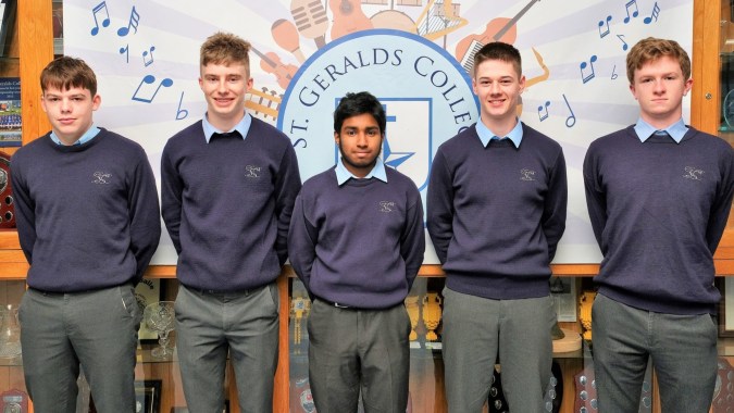 Fünf Schüler in Schuluniformen stehen vor einem Wandgemälde mit dem Logo und musikalischen Noten auf dem Gelände von St. Gerald's College.