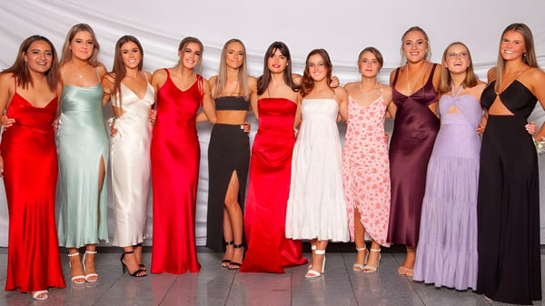 Eine Gruppe von Schülerinnen in verschiedenen festlichen Kleidern posiert vor weißem Hintergrund auf dem Campus der St. Hilda's Collegiate School.