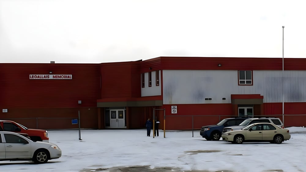 Das rote Backsteingebäude der St. James' Regional High steht vor einem verschneiten Parkplatz mit geparkten Fahrzeugen.