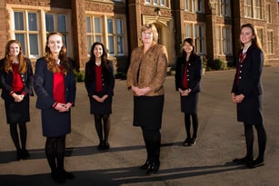 Eine Gruppe von fünf formell gekleideten Frauen steht vor dem historischen Backsteingebäude der St. James’ School.
