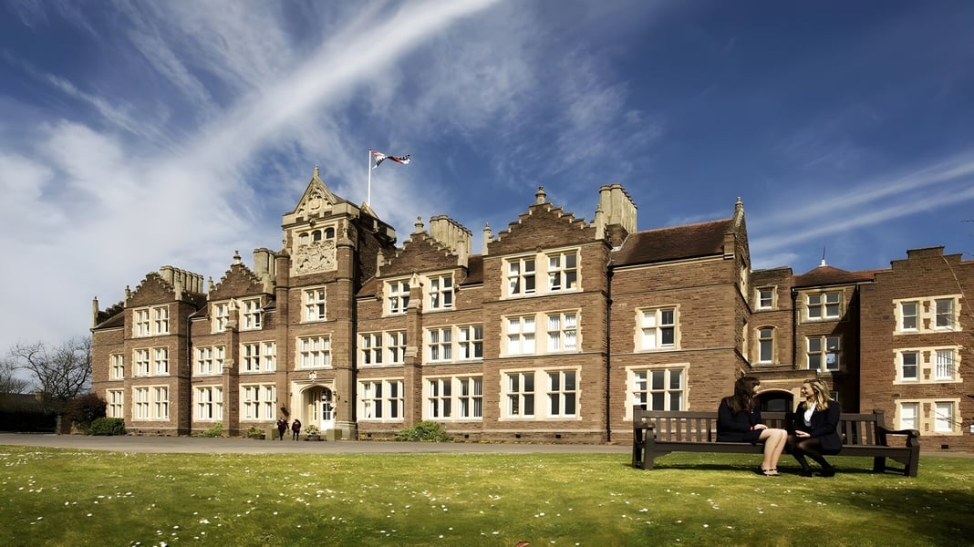 Das historische Gebäude der St. James’ School steht auf einem Grasfeld unter blauem Himmel.