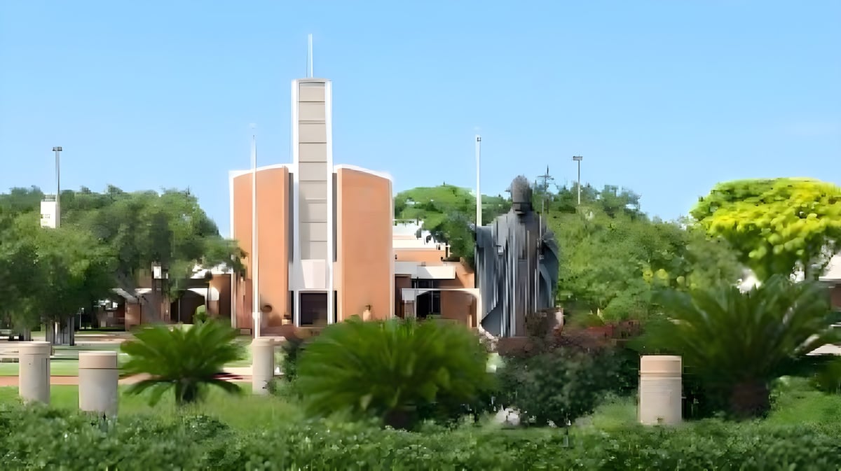 Das moderne Gebäude der St. John Paul II High School steht mit einem hohen Turm im Grünen mit Palmen und weiterer Vegetation.