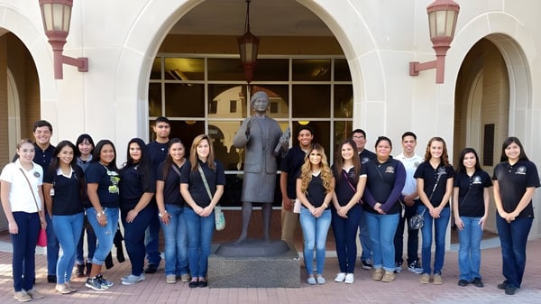 Eine Gruppe Schülerinnen und Schüler posiert vor dem Gebäude der St. John Paul II High School mit Bögen und dekorativer Beleuchtung.