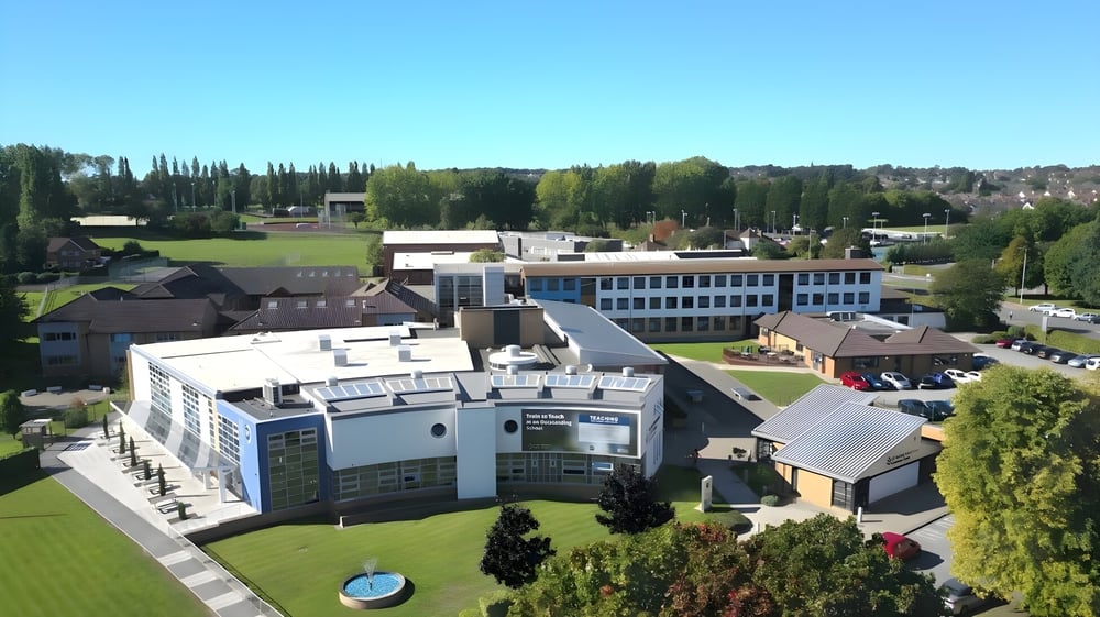Das weitläufige Gelände des St. John Plessington Catholic College mit modernen Gebäuden und grüner Umgebung unter klarem Himmel.
