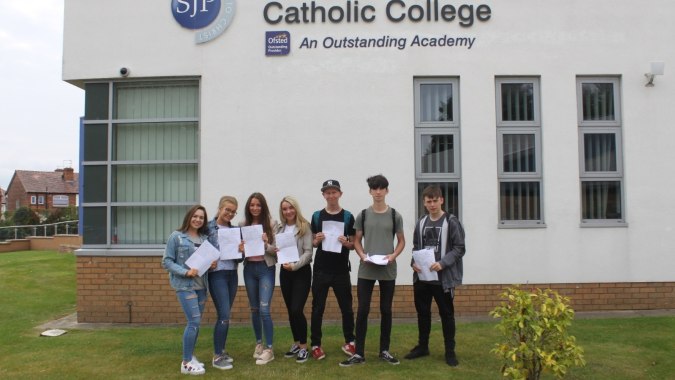 Eine Gruppe Schülerinnen und Schüler steht vor dem Gebäude des St. John Plessington Catholic College auf einer Rasenfläche.