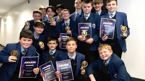 Eine Gruppe Schüler des St. John Plessington Catholic College posiert im Flur mit verschiedenen Auszeichnungen und Trophäen.