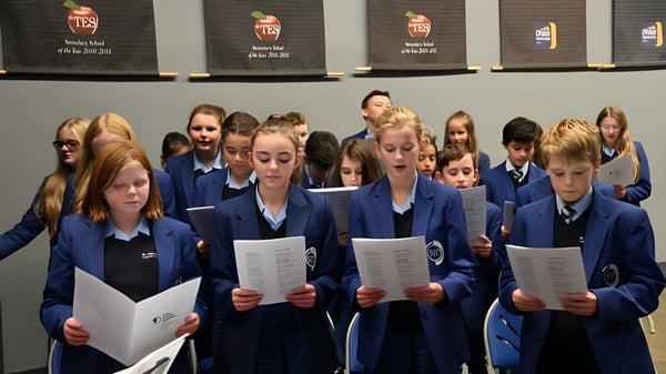 Schüler des St. John Plessington Catholic College stehen in Schuluniform vor Regalen mit Büchern und Materialien.