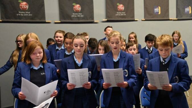 Schüler des St. John Plessington Catholic College stehen in einer Reihe und halten Papiere vor Postern an der Wand.