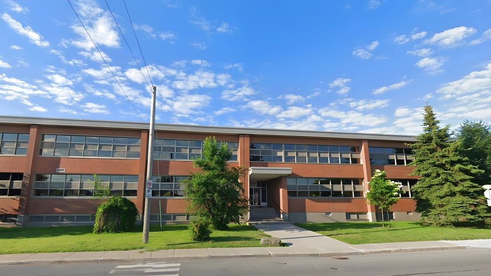 Das mehrstöckige Backsteingebäude der St. Johns High School steht auf einer Wiese mit Bäumen unter blauem Himmel.