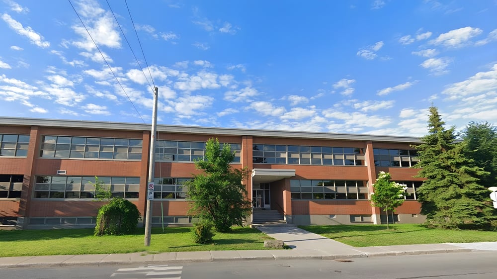 Das mehrstöckige Backsteingebäude der St. Johns High School steht auf einer Wiese mit Bäumen unter blauem Himmel.