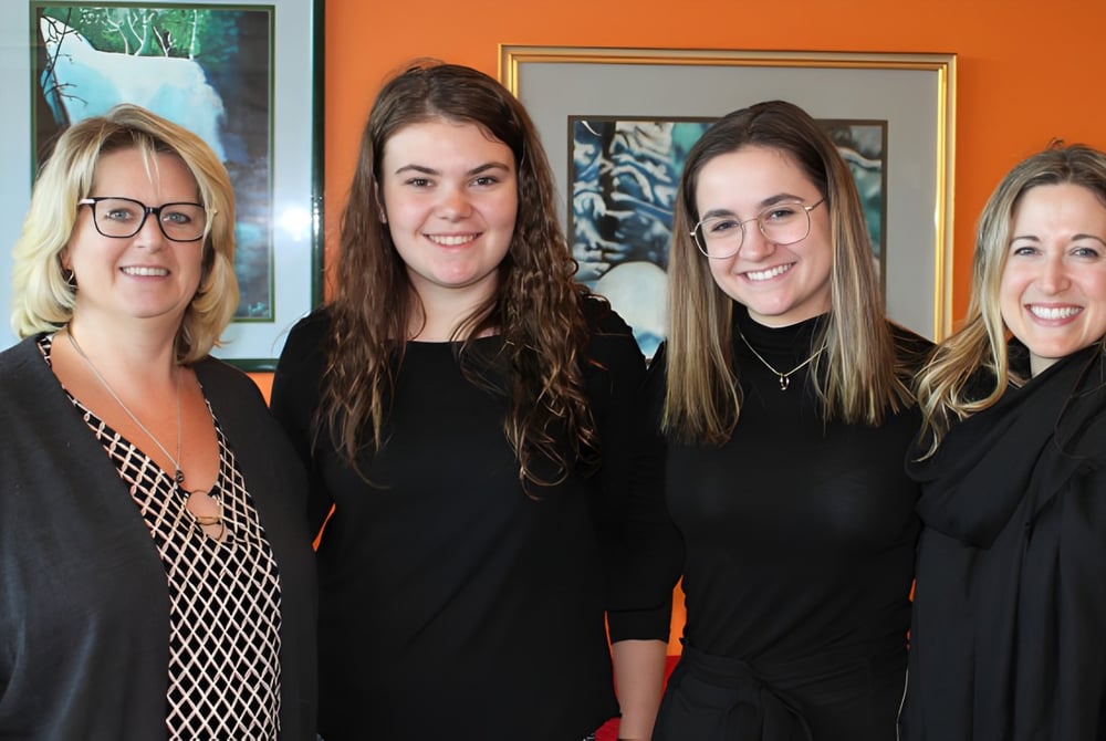 Vier Frauen posieren vor einer orangefarbenen Wand auf dem Campus der St. Johns High School.