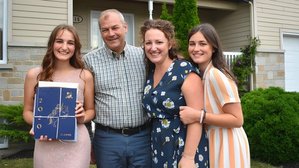 Eine Familie mit zwei Erwachsenen und zwei jungen Frauen steht vor einem Wohnhaus auf dem Gelände der St. Johns High School.