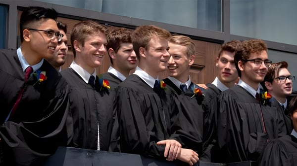 Eine Gruppe junger Männer in Abschlussroben steht vor einem Gebäude auf dem Campus der St. John’s-Kilmarnock School.