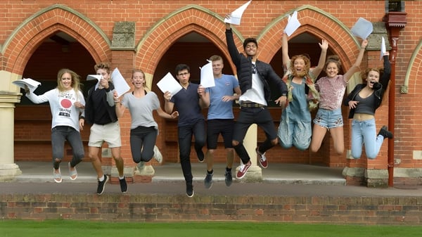 Eine Gruppe Schülerinnen und Schüler der St. John’s School in Leatherhead springt vor einem Backsteingebäude mit bogenförmigen Türen.