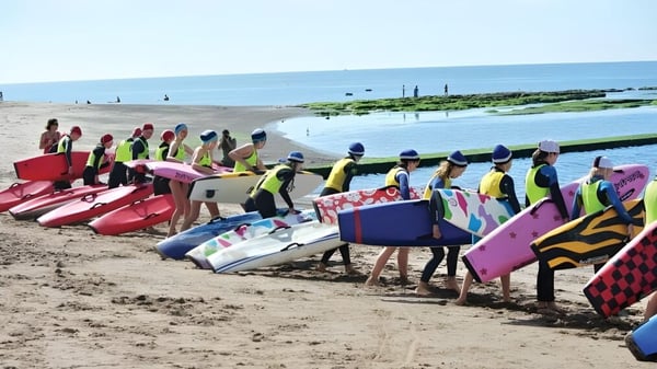 Eine Gruppe Schülerinnen und Schüler der St. John’s School am Strand trägt bunte Schwimmwesten und steht vor dem Meer.