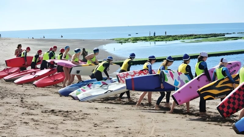 Eine Gruppe Schülerinnen und Schüler der St. John’s School am Strand trägt bunte Schwimmwesten und steht vor dem Meer.