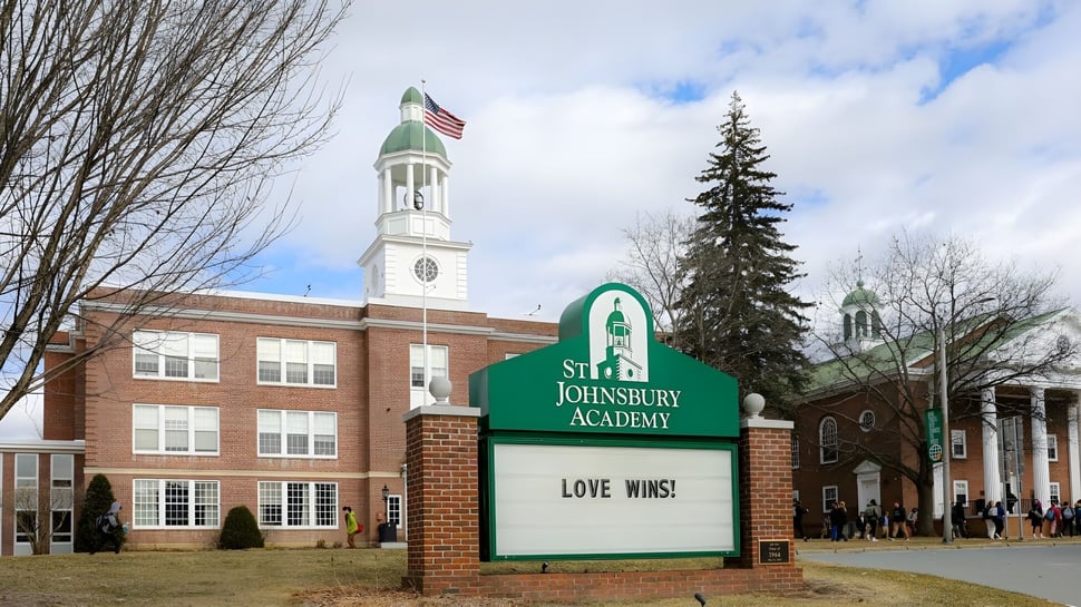 Das Backsteingebäude mit Uhrenturm und amerikanischer Flagge auf dem Campus der St. Johnsbury Academy umgeben von Bäumen und Wiese.