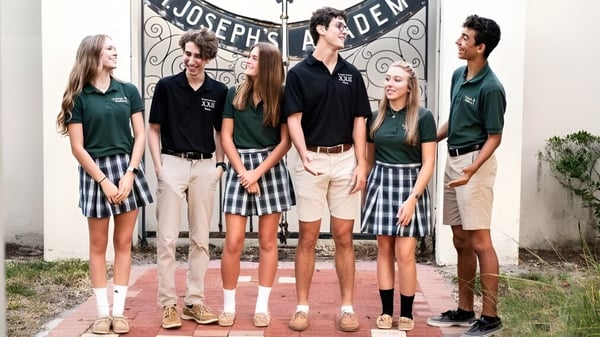 Eine Gruppe von Schülerinnen und Schülern steht vor dem Gebäude der St. Joseph Academy mit dem Schriftzug Joseph's Den.