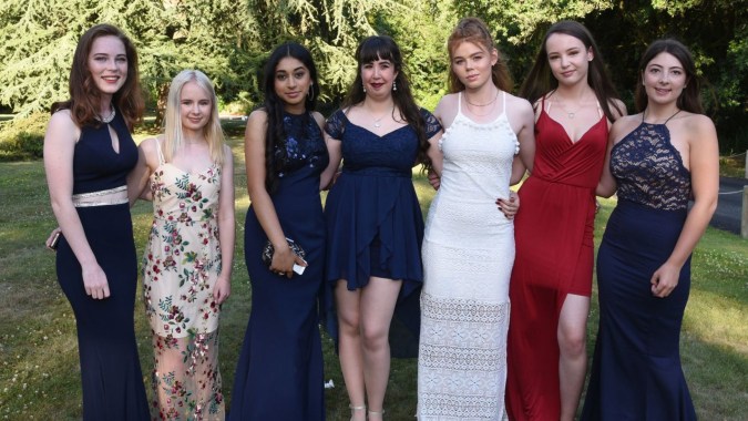 Sechs Schülerinnen der St. Joseph of Cluny School stehen in formellen Kleidern gemeinsam in einer grünen Außenanlage.