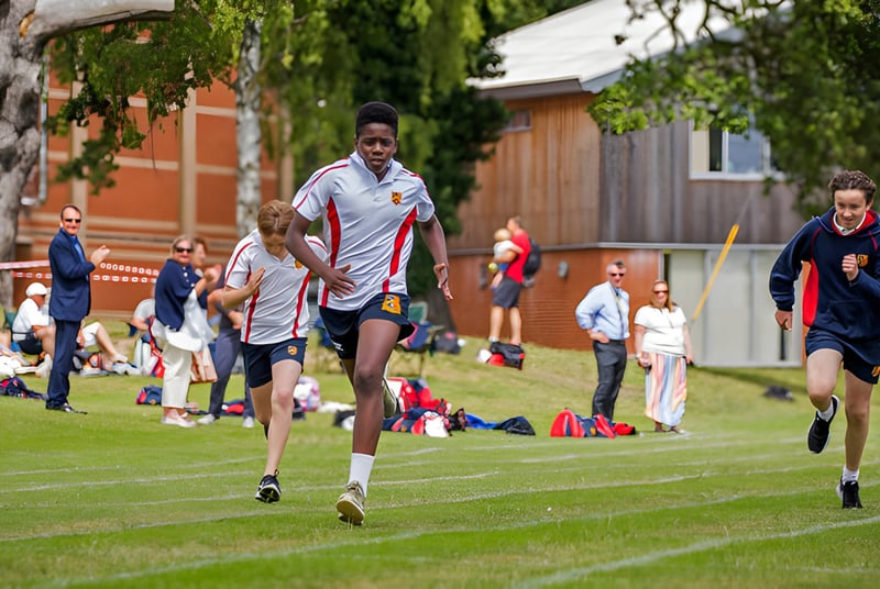 Eine Gruppe von Athleten läuft auf dem Sportfeld des St. Joseph's College vor einem Backsteingebäude.