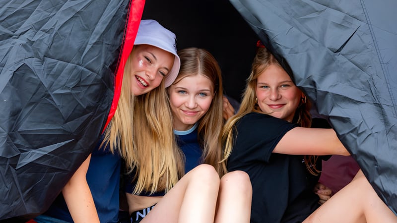 Drei Schülerinnen mit langen blonden Haaren sitzen gemeinsam in einem zeltartigen Bau mit rotem Inneren auf dem Campus von St. Joseph's College.