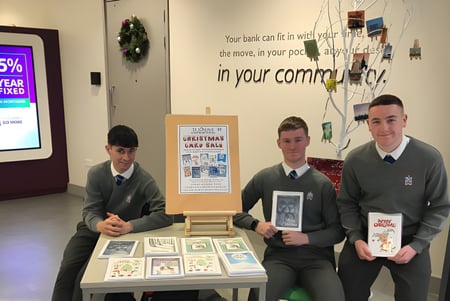 Drei Schüler in Uniform stehen hinter einem Ausstelltisch mit verschiedenen Gegenständen auf dem Campus der St. Joseph's Secondary School.