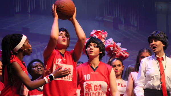 Eine Gruppe Schülerinnen und Schüler der St. Joseph’s Secondary School in Castlebar steht mit roten Trikots und einem Basketball auf einer Bühne vor einem bunten Hintergrund.