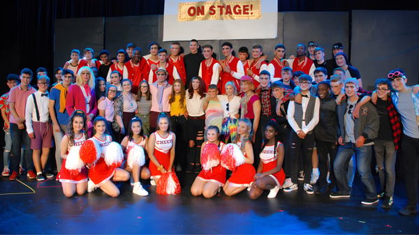 Eine Gruppe von Schülerinnen und Schülern der St. Joseph’s Secondary School steht in bunten Kostümen auf einer Bühne mit einem On Stage! Schild im Hintergrund.