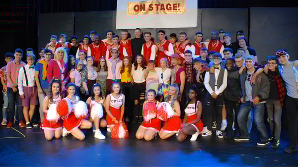 Eine Gruppe von Schülerinnen und Schülern der St. Joseph’s Secondary School steht in bunten Kostümen auf einer Bühne mit einem On Stage! Schild im Hintergrund.