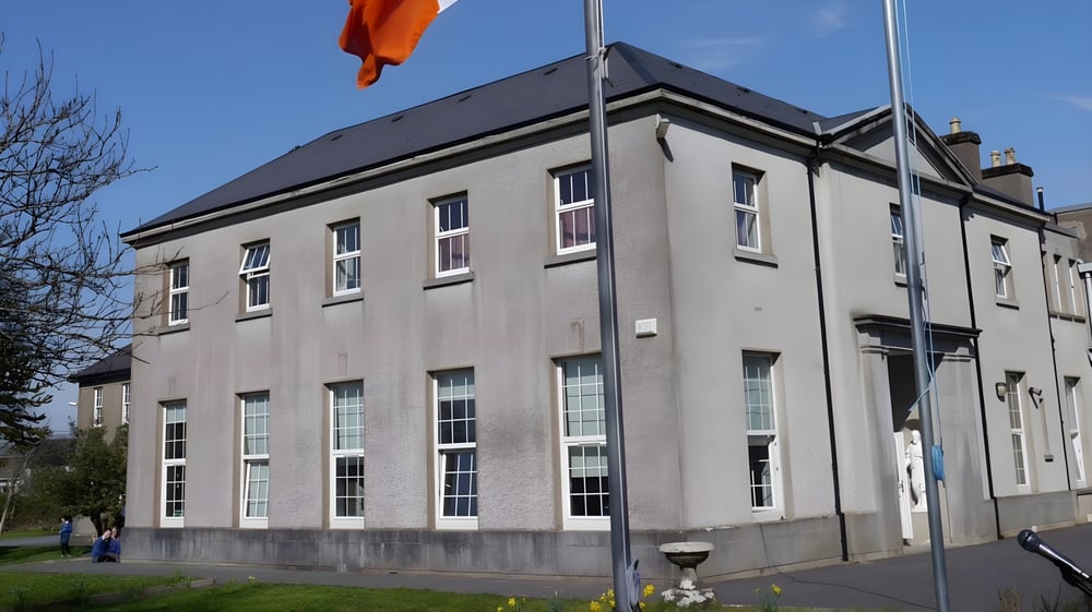 Das mehrstöckige Gebäude der St. Joseph’s Secondary School in Castlebar mit einer orangenen Flagge vor blauem Himmel.