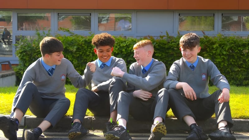 Vier Schülerinnen und Schüler der St. Joseph's Secondary School sitzen gemeinsam auf einer Bank vor einem Gebäude mit großen Fenstern.