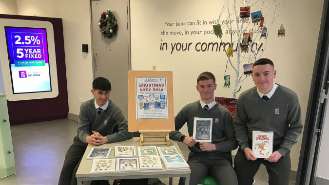 Drei Schüler in Schuluniform stehen vor einem Tisch mit verschiedenen Exponaten auf dem Gelände der St. Joseph's Secondary School.