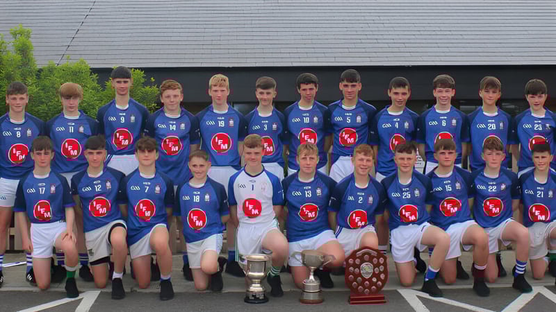 Eine Gruppe junger Athleten in blauen Trikots posiert mit Trophäen vor einem Gebäude auf dem Gelände der St. Joseph's Secondary School.