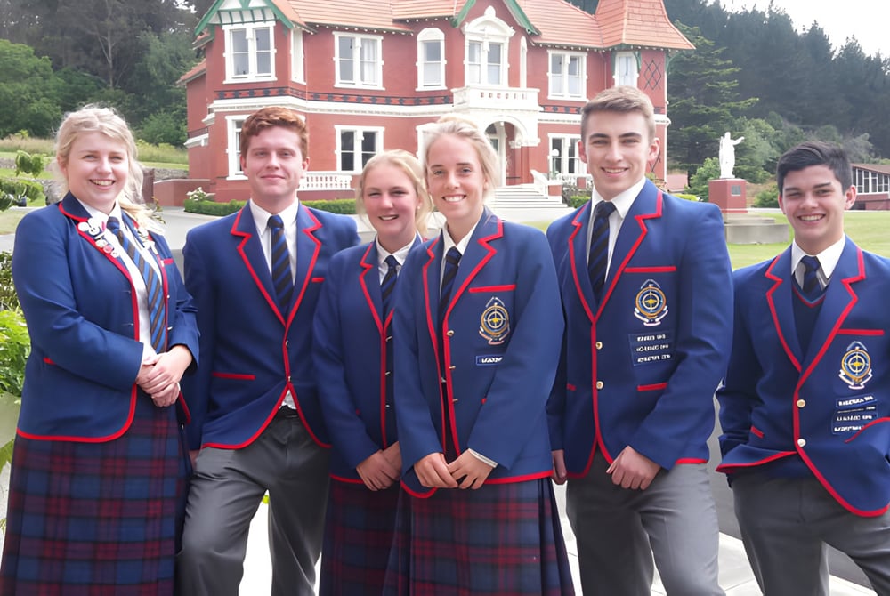 Eine Gruppe von Schülerinnen und Schülern des St. Kevin’s College posiert vor einem großen roten und weißen Gebäude mit viel Grün drumherum.