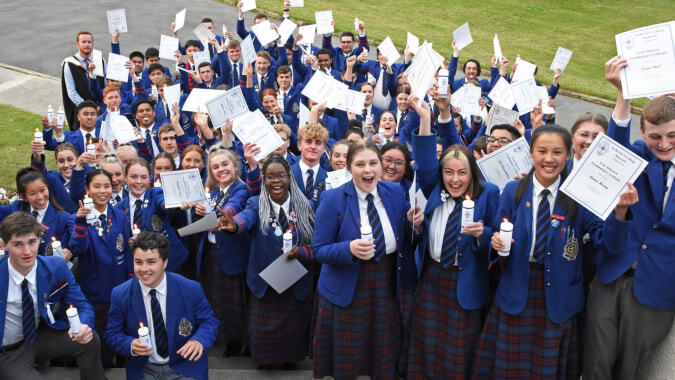 Schüler des St. Kevin’s College halten draußen Schilder und Urkunden bei einem Gruppenfoto.