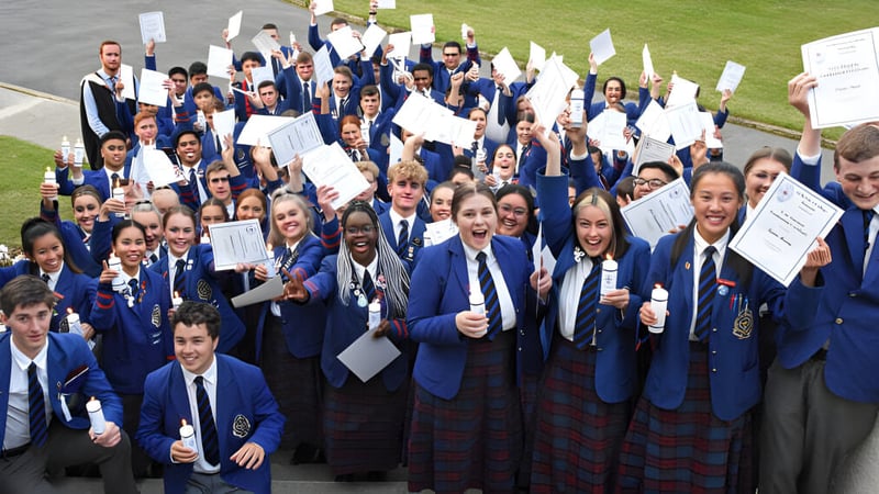 Eine große Gruppe von Schülern des St. Kevin’s College in Schuluniform hält Schilder und Papiere bei einer Versammlung im Freien.