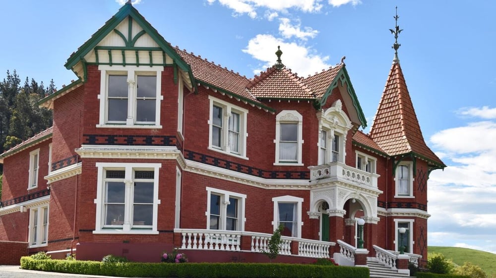 Das viktorianische Herrenhaus auf dem Campus von St. Kevin’s College mit rotem Backstein und grüner Landschaft im Hintergrund.