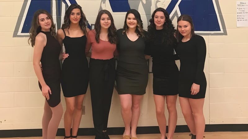 Sechs Schülerinnen der St. Kevin's High School in schwarz-roten Outfits vor blau-weißem Hintergrund.